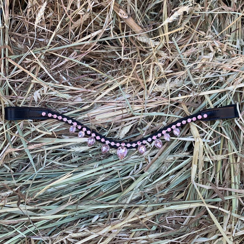 Vista de frente de nuestra **frontalera brillantes rosas**, destacando el diseño de la hilera central y los colgantes sobre el fondo natural de la paja.