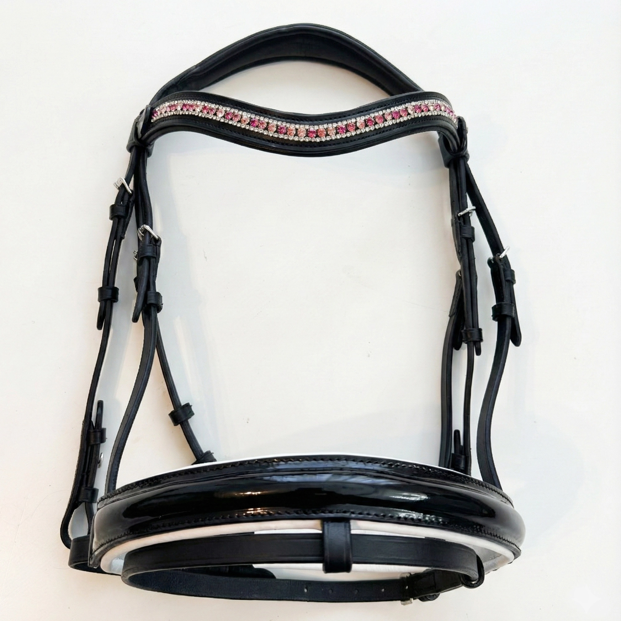 Vista completa del conjunto de doma premium, mostrando la cabezada de charol negro con la frontalera de brillantes rosa efecto degradado ya montada.